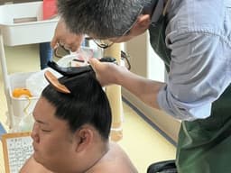A sumo wrestler gets his hair styled in a top-knot as a demo for the guests